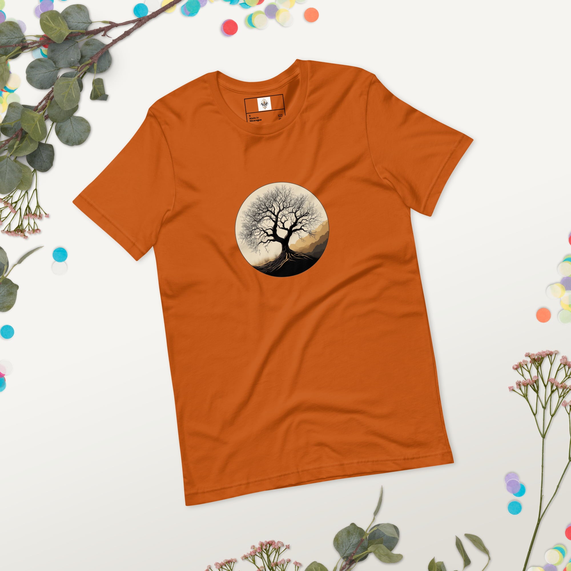 Roots of Life - Silhouette illustration of a bare tree with extensive roots, enclosed within a circle, featuring earthy tones and gentle mountains in the background. Graphic printed on autumn-colored Unisex Staple T-Shirt Bella + Canvas 3001