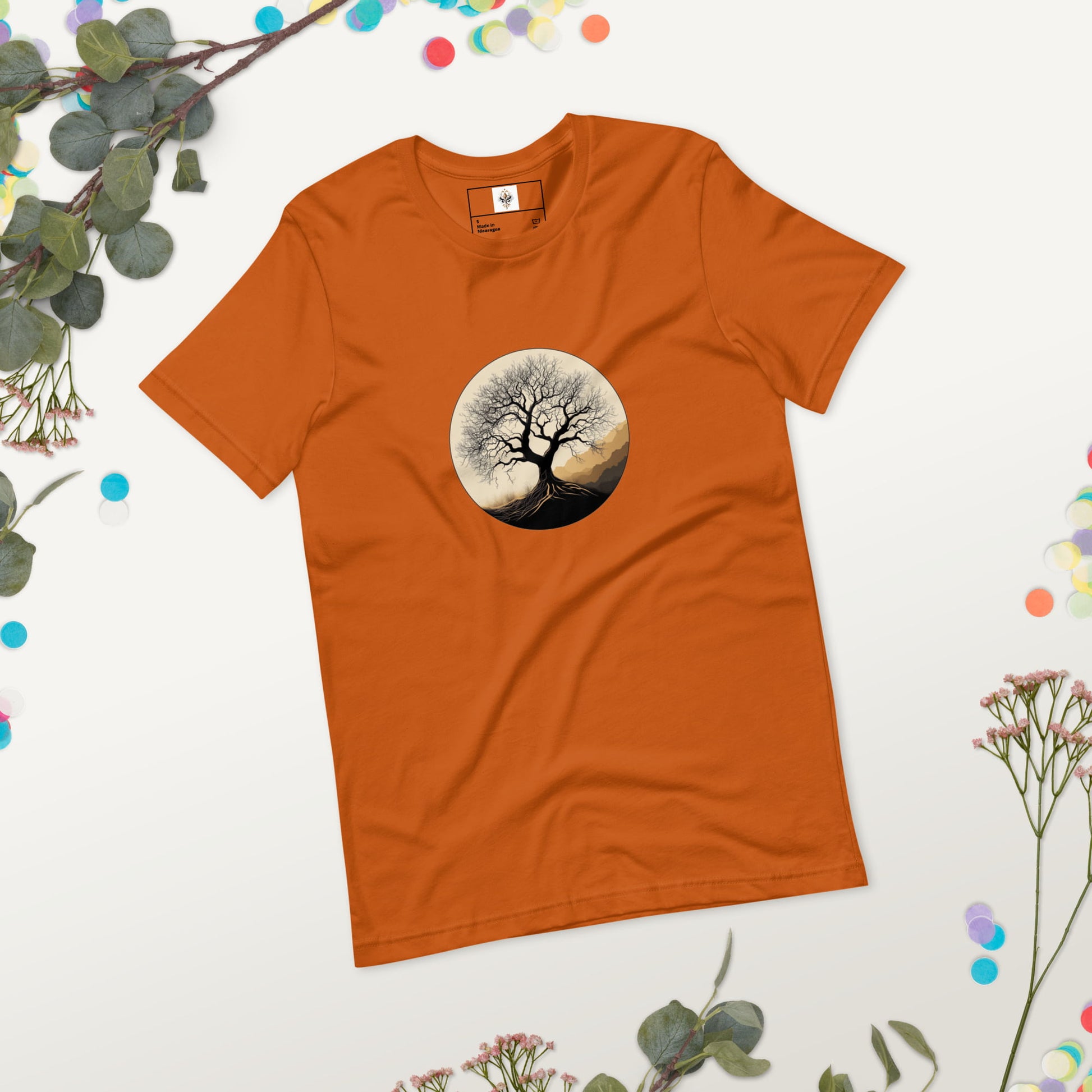 Roots of Life - Silhouette illustration of a bare tree with extensive roots, enclosed within a circle, featuring earthy tones and gentle mountains in the background. Graphic printed on autumn-colored Unisex Staple T-Shirt Bella + Canvas 3001